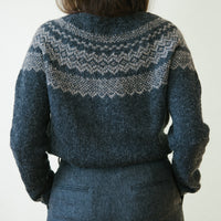 A woman wearing a dark grey handknitted sweater, seen from the back