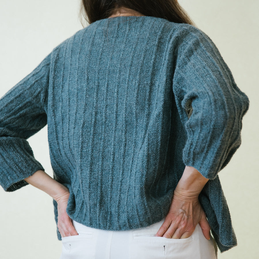 A woman wearing a handknitted cardigan, details seen from the back