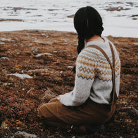 A young girl sitting on the beach wearing a handknitted sweater, seen from the back