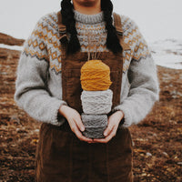 A young girl standing on the beach wearing a handknitted sweater, seen from the front