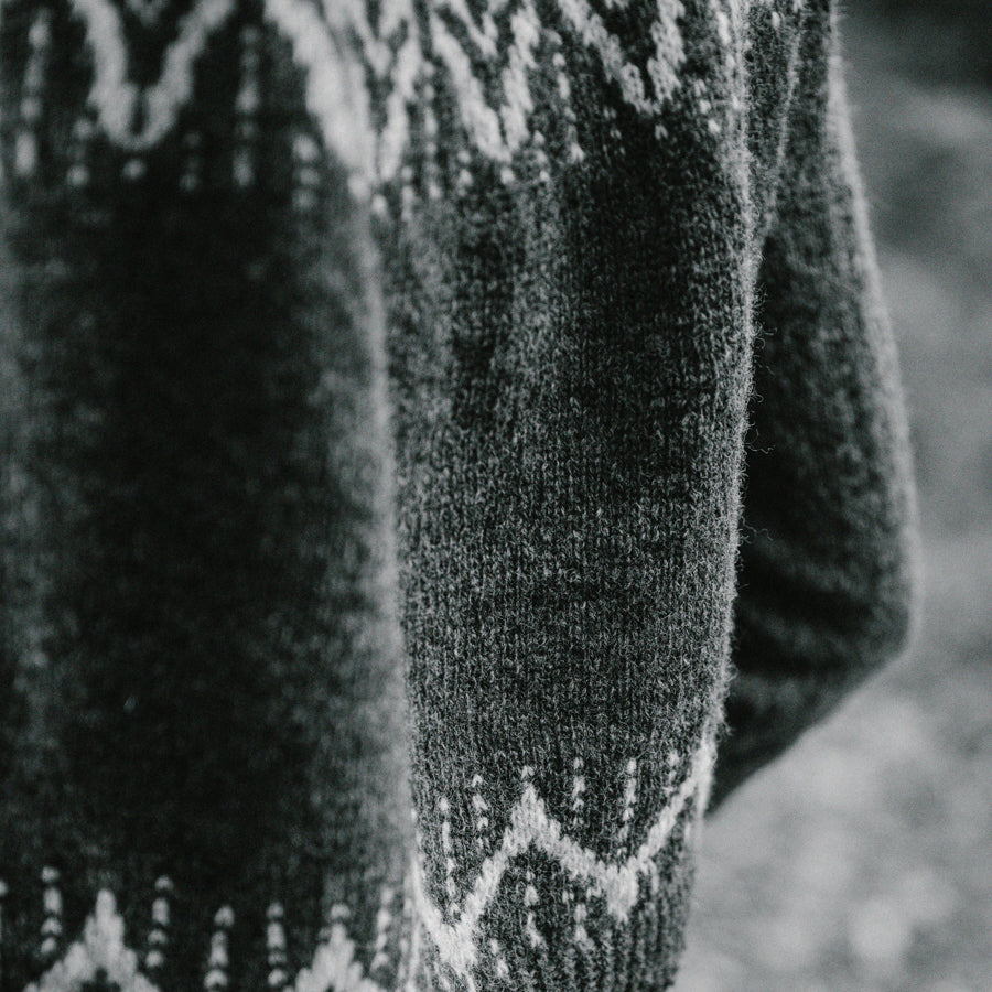 A young woman in the forest wearing a dark green handknitted sweater, details seen from the back