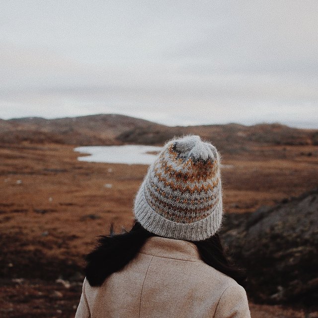 A young woman in a harsh landscape wearing a handknitted hat, seen from the back