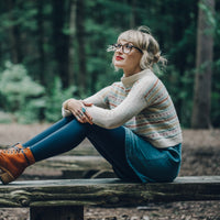 Andrea Mowry is sitting in the woods, wearing a stranded handknitted sweater