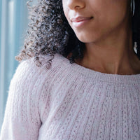A young woman is wearing a handknitted sweater in very light pink, details seen from the front